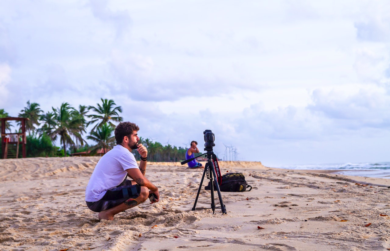 A man on a beach setting a camera on a tripod for a live stream